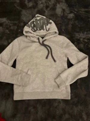 Ljusgrå hoodie med huva och ficka - Säljer en stilren ljusgrå hoodie med huva och dragsnören. Hoodien har en klassisk känguruficka framtill och ribbade muddar vid ärmar och nederkant. Perfekt för en avslappnad och bekväm look.