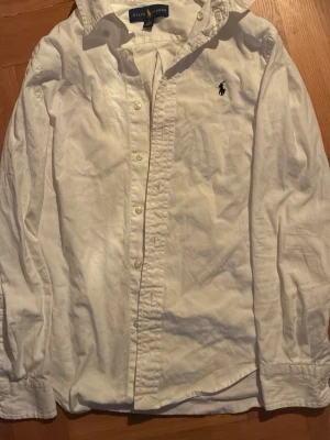 Vit skjorta från Ralph Lauren - Klassisk vit skjorta från Ralph Lauren med lång ärm och knäppning framtill. Skjortan har en broderad logga på bröstet och är tillverkad i bomull. Perfekt för en stilren och tidlös look.