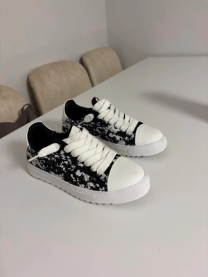 Numeris Svarta och vita  - Säljer ett par snygga sneakers i svart och vitt med coolt stänkmönster. Jag har använt de 2 gånger. Skorna har breda vita snören och tåparti i vitt med struktur. Perfekta för dig som vill sticka ut med din stil. 