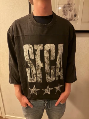 Oversized svart t-shirt med tryck - Cool oversized svart t-shirt med stort vitt SFCA-tryck och tre stjärnor framtill samt tre stjärnor på ryggen. Tröjan har 3/4-ärmar och ribbad halsringning. Perfekt för en avslappnad och trendig stil.