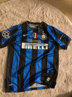 Inter Milan matchtröja Nike blå/svart - Säljer en officiell Inter Milan matchtröja från Nike i blått och svart med vertikala ränder. Tröjan har Pirelli-logga, klubbmärke, Champions League-märke och detaljer om finalen i Madrid 2010. Tillverkad i Dri-FIT material för bästa komfort.