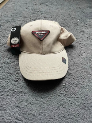 Beige keps  - Snygg beige keps från  med det klassiska trekantiga logotypmärket framtill. Kepsen har böjd skärm och justerbar passform. Tillverkad i slitstarkt tyg som passar perfekt till streetwear eller en clean look.