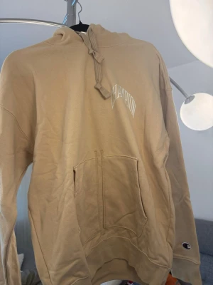 Beige hoodie från Champion XS - Snygg beige hoodie från Champion i storlek XS. Hoodien har en stor magficka, dragsko i huvan och Champion-logga på bröstet samt ärmen. Tillverkad i mjukt bomullsmaterial som är skönt att ha på sig. Perfekt för en chill och avslappnad stil.