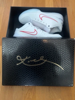 Titel:Nike Kobe IV Protro “Draft Pack” – Toronto Raptors (IV6585-900) - Nike Kobe IV Protro från “Draft Pack”-kollektionen 2026, inspirerad av Kobe Bryants proffsdebut i 1996 års NBA-draft. Denna variant motsvarar Pick #2 (Toronto Raptors) och levereras i den vita wear-away-överdelen som gradvis avslöjar lagfärgerna under användning. Skorna är en del av den randomiserade mystery-releasen med 14 färgvarianter totalt (13 wear-away + Lakers purple/gold). Originalförpackning med Kobe-signatur ingår.