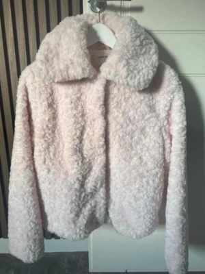 Ljusrosa teddyjacka med stor krage - Supermjuk teddyjacka i ljusrosa med oversized krage och långa ärmar. Jackan har fluffig struktur och är perfekt för att hålla värmen under kyliga dagar. Stängs framtill och har en trendig, avslappnad passform.