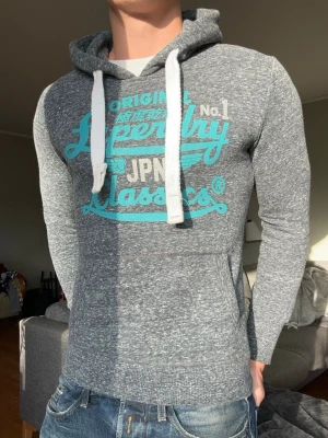 Grå Superdry hoodie - Snygg superdry hoodie med feta färger! Den är i princip i nyskick🤩Storlek S, passar som XS, modellen är 177cm lång! Tveka inte på att skicka prisförslag eller ställa frågor!😁
