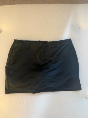Svart kjol i skinnimitation från SHEIN - Säljer en svart, tight minikjol i skinnimitation från SHEIN. Kjolen har en enkel och stilren design utan synliga detaljer, perfekt för att matcha med olika toppar och accessoarer.