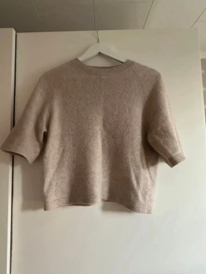 Beige stickad tröja från & Other Stories - Mysig beige stickad tröja från & Other Stories med rund halsringning och halvlånga ärmar. Tröjan har en mjuk och fluffig känsla, perfekt för lager på lager. Enkel och stilren design som passar till det mesta.