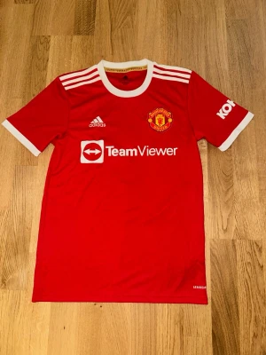Manchester United t-shirt Ronaldo 7 - Röd Manchester United t-shirt från Adidas med vitt på ryggen står det Ronaldo och nummer 7. Klassisk rund hals och korta ärmar, perfekt för dig som älskar fotboll och vill visa ditt stöd. Jätte billig och jättebra skick.