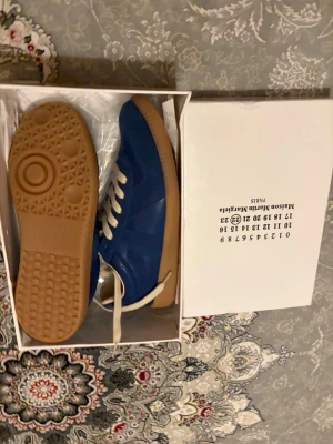 Blå sneakers med gummisula - Snygga blå sneakers med vit snörning och klassisk gummisula. Skorna har en stilren design med lågt skaft och är tillverkade i en mix av mocka och läder. Perfekta för dig som vill ha en clean och trendig look.