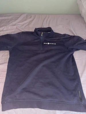 Mörkblå Sail Racing fleece med halv dragkedja - Mörkblå fleece från Sail Racing med halv dragkedja och hög krage. Tröjan har diskret logga på bröstet och är perfekt för lager-på-lager. Mjuk och skön känsla, passar till chill eller när du vill vara extra varm.