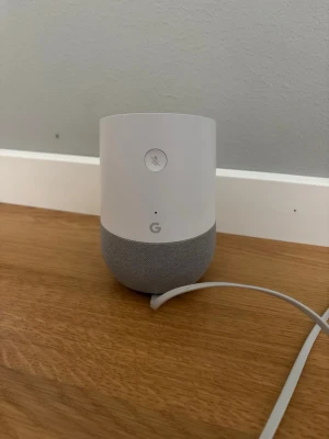 Google Home smart högtalare vit/grå - Säljer en Google Home smart högtalare i stilren vit och ljusgrå design. Högtalaren har rund form, tygklädd nedre del och medföljande strömadapter. Perfekt för att styra musik och smarta hemmet med röststyrning. Nästan helt oanvänd, pris kan diskuteras 