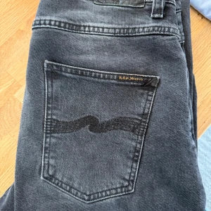Grå/svarta jeans från Nudie Jeans - Snygga gråsvarta jeans från Nudie Jeans med klassisk femficksdesign och broderad bakficka. Modellen heter Grim Tim.  99% bomull, 1% elastan. Knappt använda så mycket gott skick!
