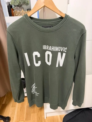 Grön ICON sweatshirt Ibrahimovic - Mörkgrön sweatshirt med trycket 'IBRAHIMOVIC ICON' i vitt framtill. Tröjan har rund halsringning, långa ärmar och ribbade muddar vid ärmslut och nederkant. Perfekt för en avslappnad och sportig stil.