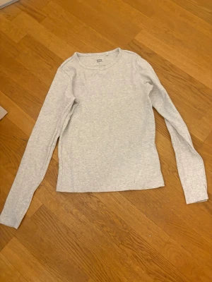 Ljusgrå långärmad topp - En enkel och stilren ljusgrå långärmad topp med rund halsringning. Perfekt att matcha med jeans eller kjol för en clean look. Tillverkad i mjukt bomullsmaterial som känns skönt mot huden.