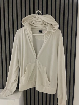 Vit hoodie med dragkedja Gina Tricot - Snygg vit hoodie från Gina Tricot i storlek L. Hoodien har dragkedja framtill, två stora fickor och en klassisk huva. Tillverkad i mjukt material som känns skönt mot huden. Perfekt för en chill och avslappnad stil.