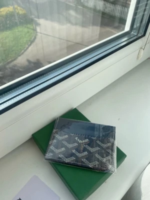Svart plånbok med mönster - Snygg svart plånbok. Plånboken är kompakt och har en stilren design, perfekt för kort och sedlar. Kommer med original grön ask och tillbehör.