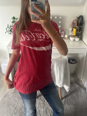 Röd Coca-Cola t-shirt - Säljer en röd Coca-Cola t-shirt med vit logga framtill. T-shirten har normal passform och korta ärmar, perfekt för en avslappnad och cool stil. Tillverkad i mjuk bomull som känns skön mot huden.