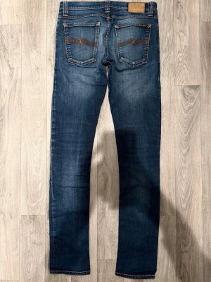 Nudie Jeans Tight Long John Blå W29/L34 - Skinny Fit - Nudie Jeans Tight Long John ”Dark Indigo” blå jeans med skinny fit-passform och låg midja, storlek W29/L34, midja 38 cm, ytterbenslängd 107 cm, benöppning 15 cm, modellen är 185cm & väger 65kg, i fint skick.