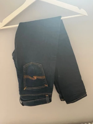 Mörkblå jeans med kontrastsömmar - Snygga mörkblå jeans med klassisk femficksdesign och tydliga kontrastsömmar på bakfickorna. Jeansen har raka ben och är tillverkade i ett robust denimtyg. Perfekta för en avslappnad och trendig stil.