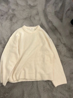 Stickad tröja Gina tricot - Mysig krämvit stickad tröja med rund halsringning och ribbade muddar vid ärmslut och nederkant. Tröjan har en avslappnad, oversized passform och är perfekt för lager på lager. Materialet ser mjukt och fluffigt ut, vilket ger en skön känsla.