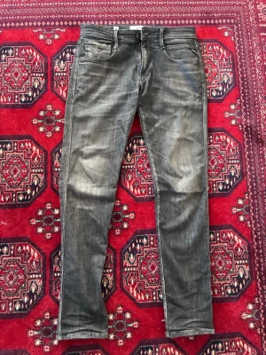 Grå slim fit jeans från Replay - Snygga grå slim fit jeans från Replay med slitna detaljer och klassisk femficksmodell. Jeansen har en något tvättad look och raka ben. Perfekta för dig som gillar en modern och avslappnad stil. Modell: Replay Anbass (organic cotton).                      Jeansen är i nyskick: 10/10 förutom ett liten hål som kan ses på sista bilden. I och med att hålet ligger så pass nära sömmen går det lätt att fixa hemma. 