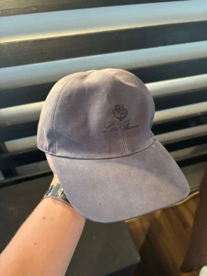 Blå keps från Loro Piana - Snygg blå keps från Loro Piana med broderad logga framtill. Klassisk sexpaneldesign och böjd skärm. Tillverkad i ett mjukt tyg som ger en avslappnad och stilren look. Perfekt accessoar för att lyfta din outfit. 