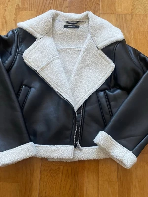 Svart teddyjacka från Gina Tricot - Säljer en svart teddyjacka från Gina Tricot i storlek XS. Jackan har vit fuskpäls på krage, ärmslut och nederkant samt dragkedja framtill. Snygg bikerinspirerad modell med två fickor och mjukt, mysigt material.