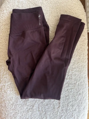 Dfyne impact espresso  - Snygga seamless leggings från Dfyne med hög midja och ribbad linning. Stretchigt material som sitter skönt och formar sig efter kroppen. Perfekta för träning. Finns ett hål som sitter i sömnen på insidan av benet