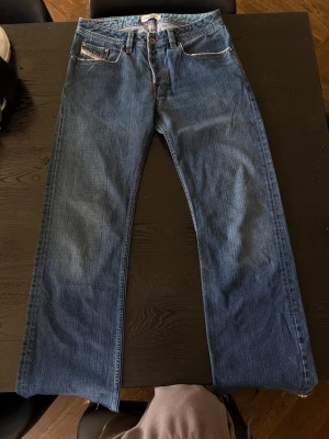 Vintage Diesel jeans - Säljer ett par vintage blå jeans från Diesel med raka ben och fem fickor. Jeansen har snygga slitningar och kontrastsömmar samt Diesel Industry-märke på myntfickan. Tillverkade i slitstark denim med cool vintagekänsla.