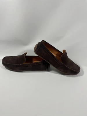 Mörkbruna mocka loafers - Säljer ett par stilrena mörkbruna loafers i mocka med klassisk design. Skorna har rundad tå, diskreta sömmar och en mjuk innersula i ljust material. Perfekta för dig som gillar en avslappnad men snygg look.