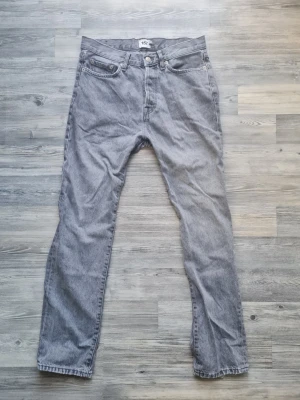 Gråa raka jeans - Säljer ett par gråa jeans med rak passform och klassisk femficksdesign. Jeansen har normal midja och stängs med knapp. Materialet är denim i bomull och färgen är en snygg ljusgrå ton som passar till det mesta. Storlek W28 L32
