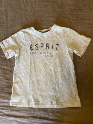 Grå t-shirt från Esprit stl.110 - Stl.110 Snygg ljusgrå t-shirt från Esprit med tryck 'ESPRIT NAUTICAL MEASURES' framtill. Barnkläder
