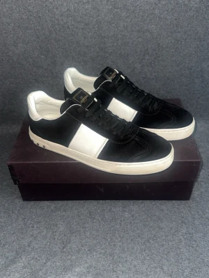 Valentino flycrew i svart mocka - Snygga sneakers i svart mocka med vita detaljer och vit sula från valentino . Skorna har en klassisk låg profil och svarta skosnören. Insidan och hälen är vita vilket ger en schysst kontrast. Strl 42 upplevs mer som 43. Perfekta för dig som gillar stilrena och tidlösa sneakers. Obs box tillkommer ej