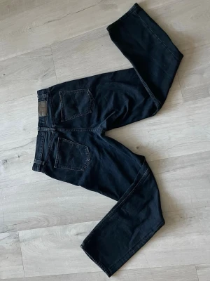 Nudie straight fit jeans - Säljer ett par mörkblåa jeans med rak passform och klassiska bakfickor. Jeansen har hög midja och är tillverkade i ett kraftigare denimtyg. Perfekta för dig som gillar en clean och enkel stil.