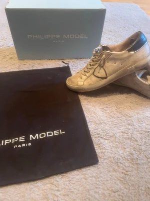 Philippe Model skor - Snygga vita sneakers från Philippe Model med svarta detaljer på hälen. Skorna har vita sulor och är tillverkade i en mix av mocka och läder. Bra kvalité på skorna, köpte dom för ett litet tag sen för 4500 och man får med boxen och dustbagen när man köper skorna. Ett snöre har gått av precis på toppen men kan enkelt fixas, hälarna har jag även fixat hos en skomakare för dom gick sönder men är normala nu bara en annan färg. Perfekta för dig som gillar stilrena och trendiga sneakers.