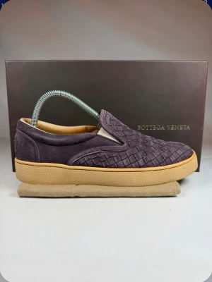 Lila slip-on sneakers Bottega Veneta - Snygga slip-on sneakers från Bottega Veneta i lila mocka och läder med det klassiska flätade mönstret. Skorna har en beige gummisula och en stilren, låg profil som passar perfekt till streetwear och casual outfits.