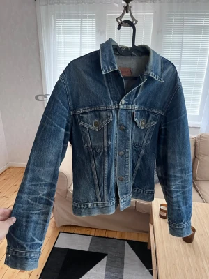 Klassisk blå jeansjacka från Levi's - Säljer en klassisk blå jeansjacka från Levi's i modell 70500. Jackan har två bröstfickor med lock och knappar, samt knappstängning framtill. Snygg tvättad denim med vintagekänsla och raka ärmar. Perfekt för dig som gillar tidlös streetstil.