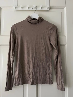 Beige polotopp från Amisu - Säljer en beige polotopp från Amisu i mjukt och tunt material. Toppen har lång ärm och en hög polokrage som ger en clean och stilren look. Perfekt att styla med jeans eller kjol för en enkel men snygg outfit.