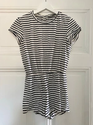 Randig kortärmad jumpsuit/playsuit - Randig jumpsuit/playsuit i storlek S, med knappar baktill i nacken. Använd endast en eller ett fåtal gånger.