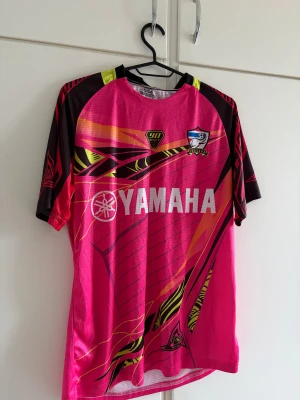  Yamaha JUL tröja - Snygg rosa sporttröja från Yamaha med JUL-tryck och grafiska detaljer i svart, gult och rött. Använd en gång. 