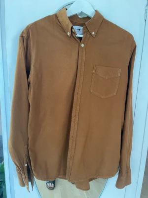 Brun manchesterskjorta från NN07 - Säljer en snygg brun manchesterskjorta från NN07 med klassisk button-down krage och bröstficka. Skjortan har långa ärmar och knappar framtill. Perfekt för dig som gillar en stilren och avslappnad look.