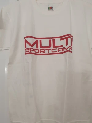 T-shirt - Vit t-shirt från Fruit of the Loom med röd MULTI SPORTCAMP-tryck på både fram- och baksidan. Klassisk passform och rund halsringning. Tillverkad i mjuk bomull, perfekt för dig som gillar sportig och enkel stil. Finns små fläckar.