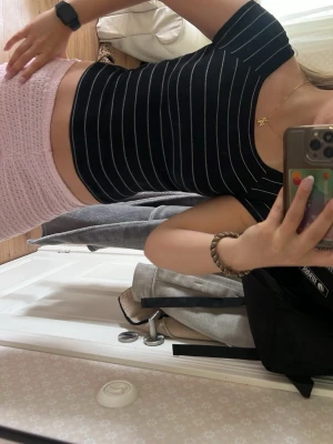Svart ribbad crop top med vita ränder - Snygg svart crop top med tunna vita vertikala ränder. Toppen har korta ärmar och en tight, kroppsnära passform. Materialet ser stretchigt och bekvämt ut, perfekt för en trendig och avslappnad look.