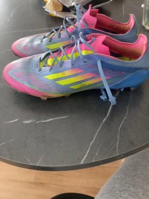 Adidas F50 elite - Säljer ett par Adidas fotbollsskor i en riktigt färgstark design med blå, rosa och gula detaljer. Skorna har klassisk låg profil, snörning och mönstrad yttersula för bra grepp på planen. Perfekta för dig som vill sticka ut på fotbollsplanen!