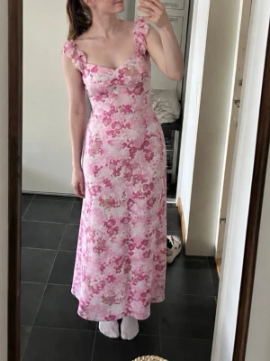 Lång klänning pieces  - Säljer en lång klänning med blommigt mönster i olika rosa och beige nyanser. Klänningen har volangprydda axelband, markerad midja och en lätt utsvängd kjol. Perfekt till sommar, brölopp eller midsommar 