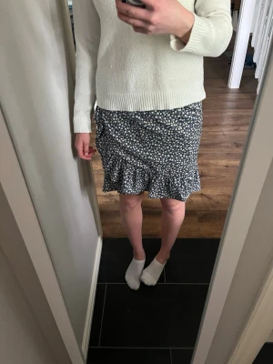 Blommig volangkjol i blått och vitt - Kort blommig kjol i blått och vitt med volangkant nertill och omlottkänsla. Kjolen har en fin siluett och är perfekt för vår och sommar. Materialet känns lätt och luftigt, troligen polyester eller bomull.