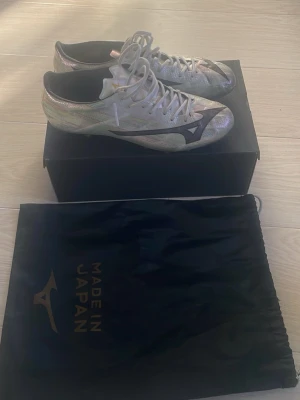 Mizuno α II Japan AG fotbollsskor 43  - Säljer ett par Mizuno α II Japan AG fotbollsskor i silver med svarta detaljer. Skorna har snörning och är tillverkade i syntetmaterial för optimal prestanda på planen. Perfekta för dig som vill sticka ut med stil och kvalitet på matchen. Nypris är 3800. Säljer pågrund ut av att de inte passade mig. Bara använd en träningsvecka