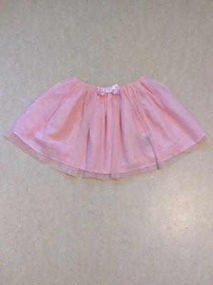 Rosa tyllkjol med rosett  - Söt rosa kortkjol i tyll med en liten rosett framtill i midjan. Kjolen har ett fluffigt utseende och passar perfekt för dig som gillar en lekfull och gullig stil.  Kjol från H&M