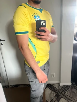 Gul Brasilien Nike fotbollströja - Snygg gul Brasilien fotbollströja från Nike med gröna detaljer och CBF-emblem på bröstet. Tröjan har korta ärmar, rund halsringning och är tillverkad i ett lätt, ventilerande material som passar perfekt till träning eller match.